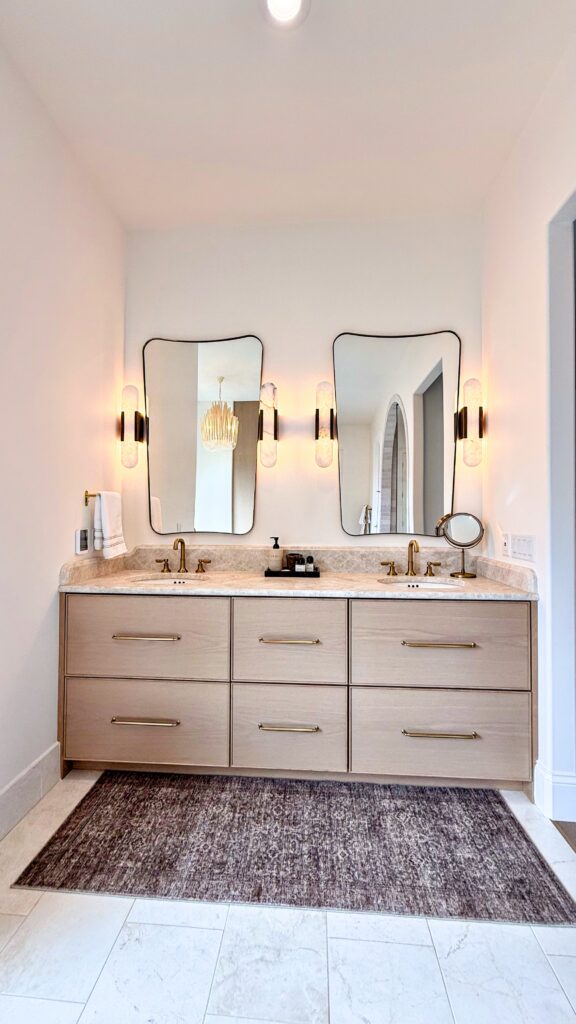 Floating light oak double vanity with six drawers, brass pulls, stone top, two undermount sinks and wavy mirrors