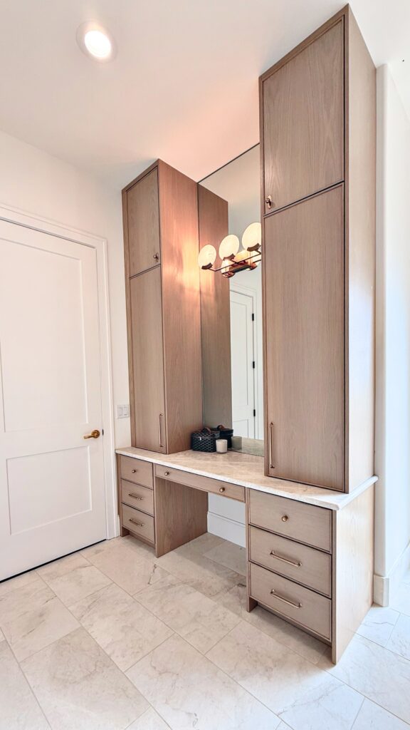 Light oak makeup vanity with tall flanking towers, stone countertop, mirror and drawer banks on marble tile floor