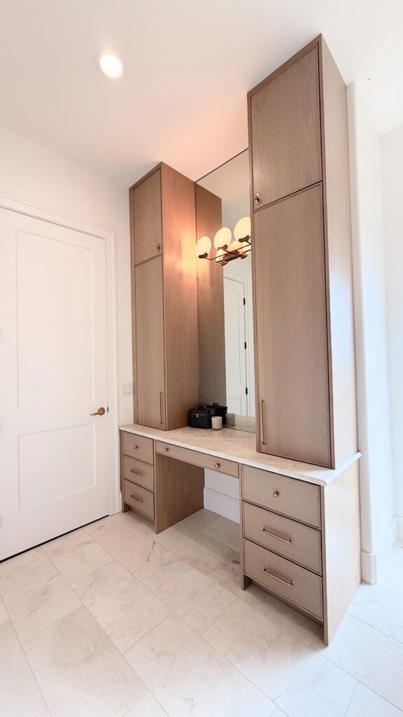 Light white oak bathroom vanity with makeup station, tall linen towers, marble top, and brass pulls