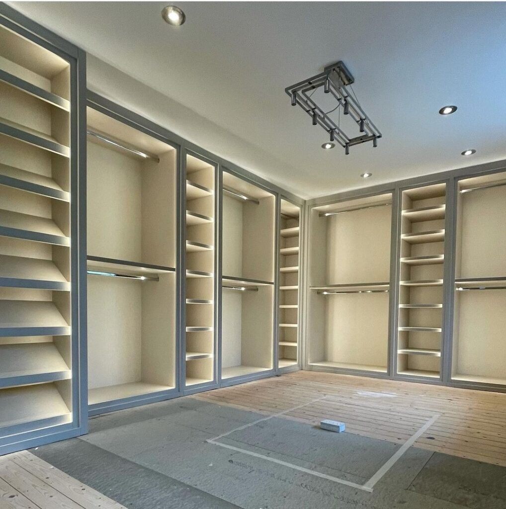 Empty built-in walk-in closet with gray framed bays, cream shelving, hanging rails, and LED strip lighting