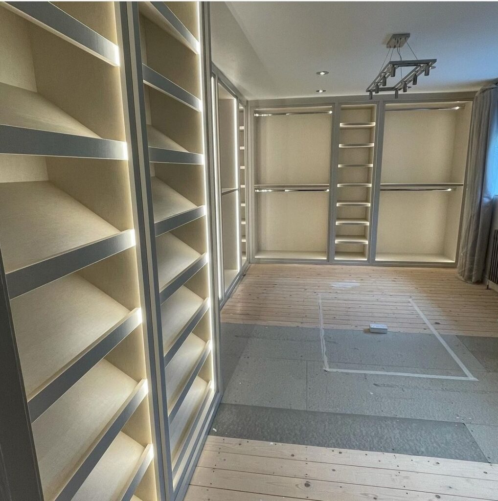 Walk-in wardrobe with cream open shelving, angled shoe racks, hanging rails and LED strip lighting