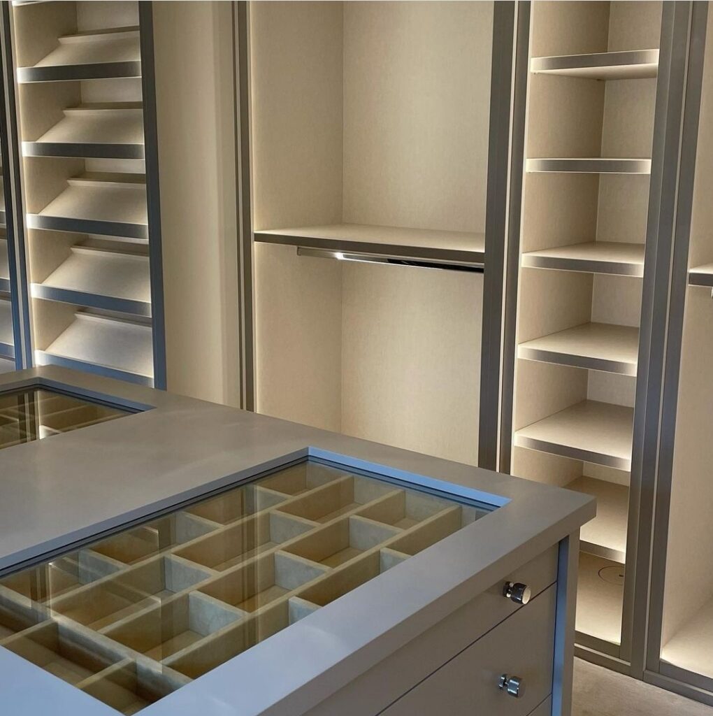 Walk-in closet with glass-top jewelry island, LED-lit shelving, hanging rail and shoe racks in cream tones