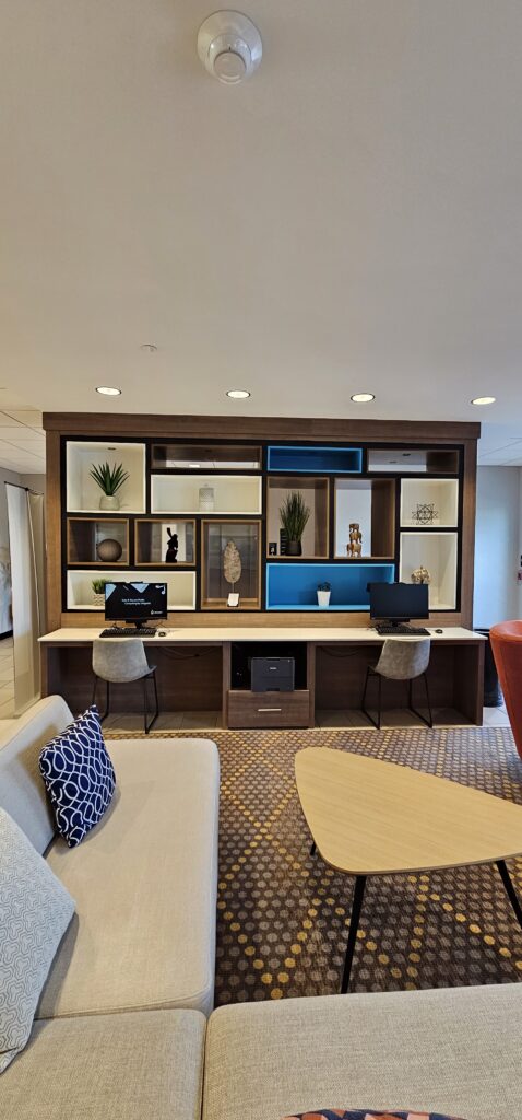 Hotel business center with dark wood wall unit, white and blue display niches, twin computer workstations and stools