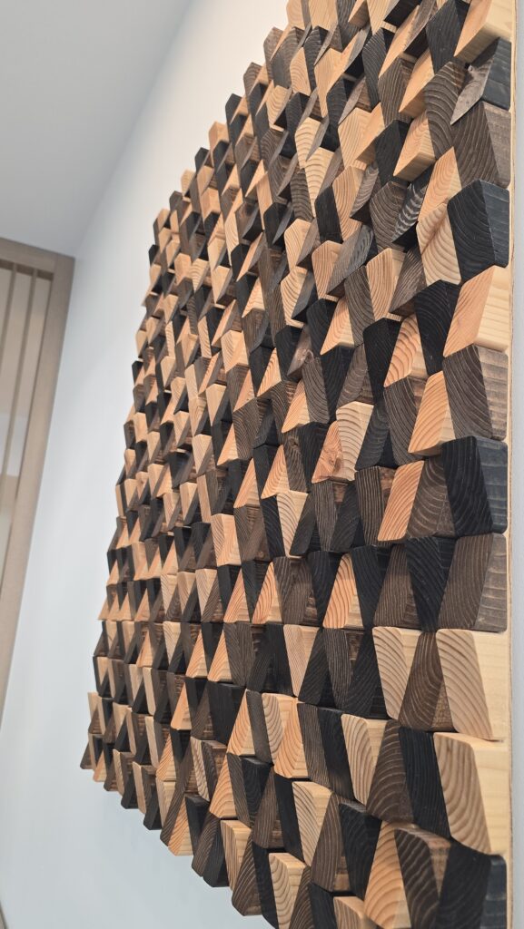 Angled view of a 3D wall panel made of hundreds of bevelled wood blocks in natural, charred and dark tones