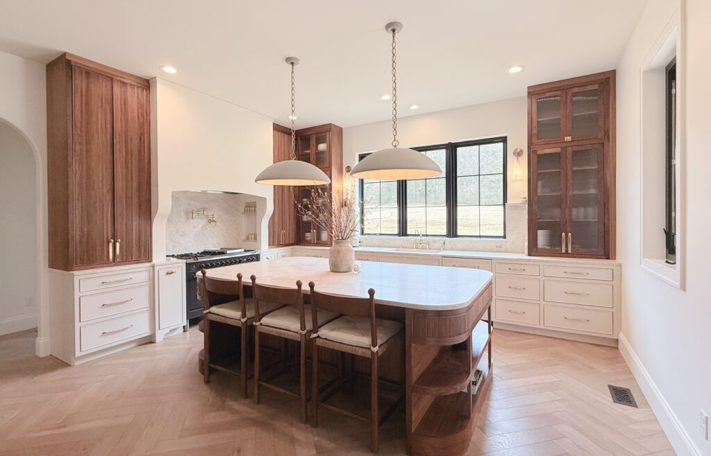 Two-tone kitchen with walnut upper cabinets, cream base drawers, curved walnut island and marble countertop