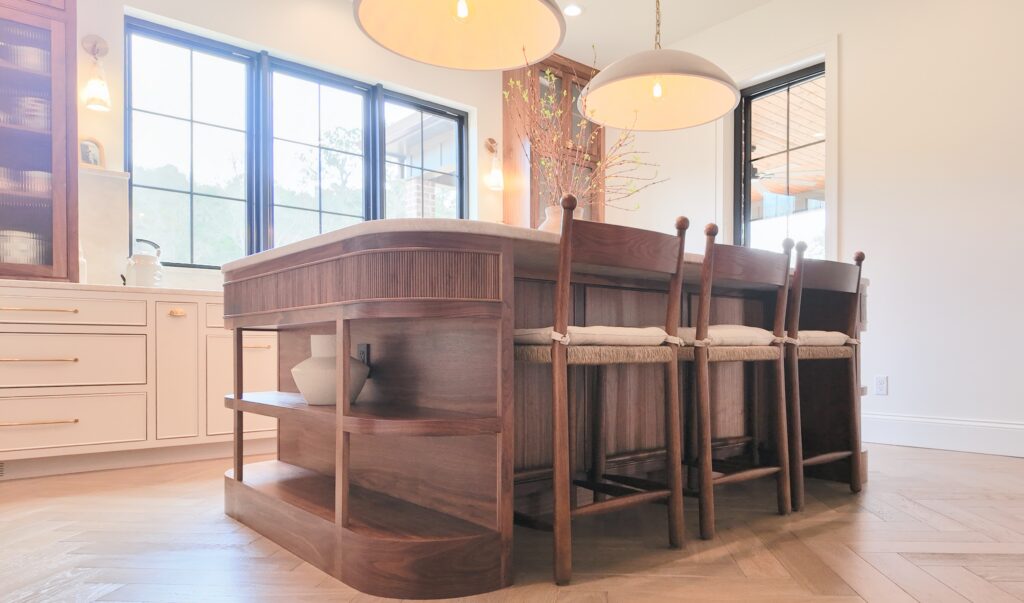 Curved walnut kitchen island with fluted panel, open end shelves, rush-seat stools on herringbone wood floor
