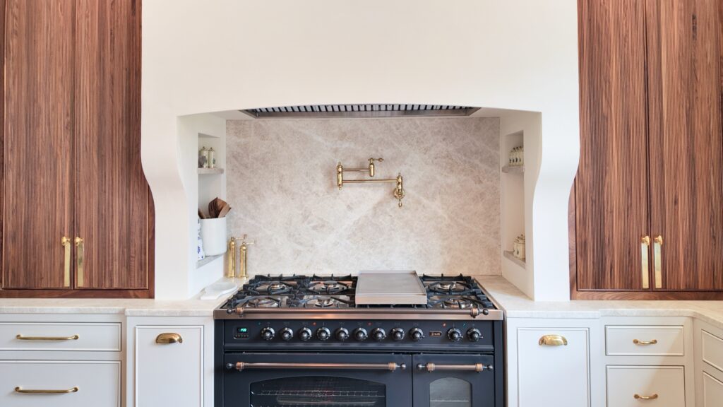 Plastered range alcove with marble backsplash, brass pot filler, navy range cooker, walnut and cream cabinets
