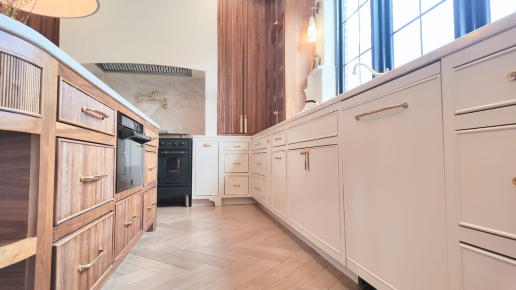 Kitchen with cream shaker base cabinets, ribbed wood island, walnut tall units, navy range and herringbone floor