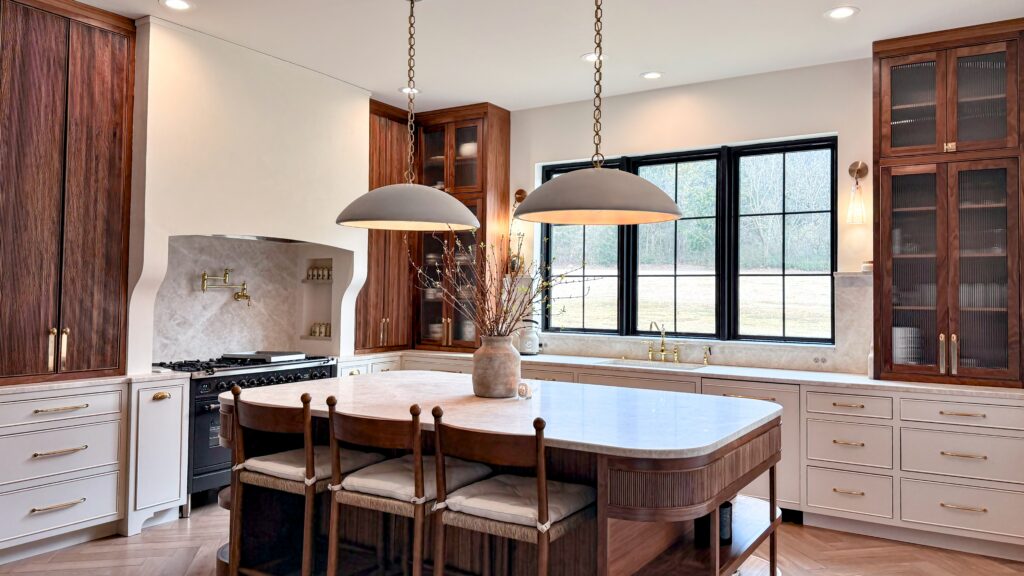 Kitchen with cream perimeter cabinets, walnut tall units, fluted island with marble top and two dome pendants