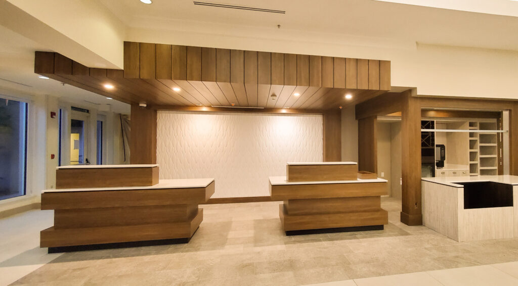 Two wood-clad hotel reception desks with white stone tops under a slatted wood ceiling and textured feature wall.
