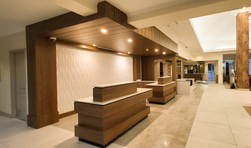 Hotel lobby with two wood-clad reception desks, slatted wood ceiling soffit and textured white wall panel